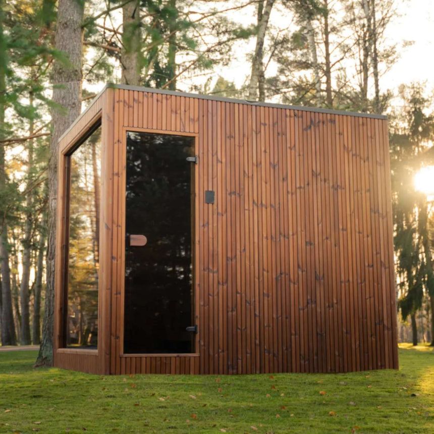 Celsium Jonas Grand outdoor sauna with its full-height tinted glass door and vertical ThermoWood cladding at sunset
