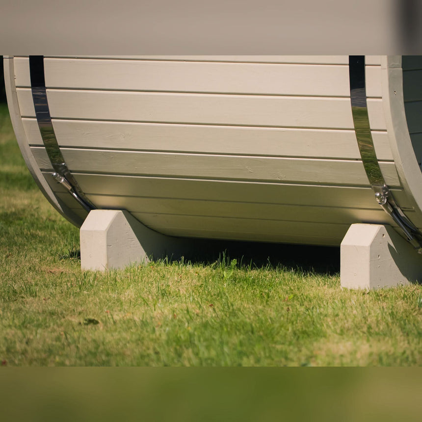 Rounded base of a light-colored Celsium Ula Mini outdoor sauna resting on two supports, with metal bands at each end