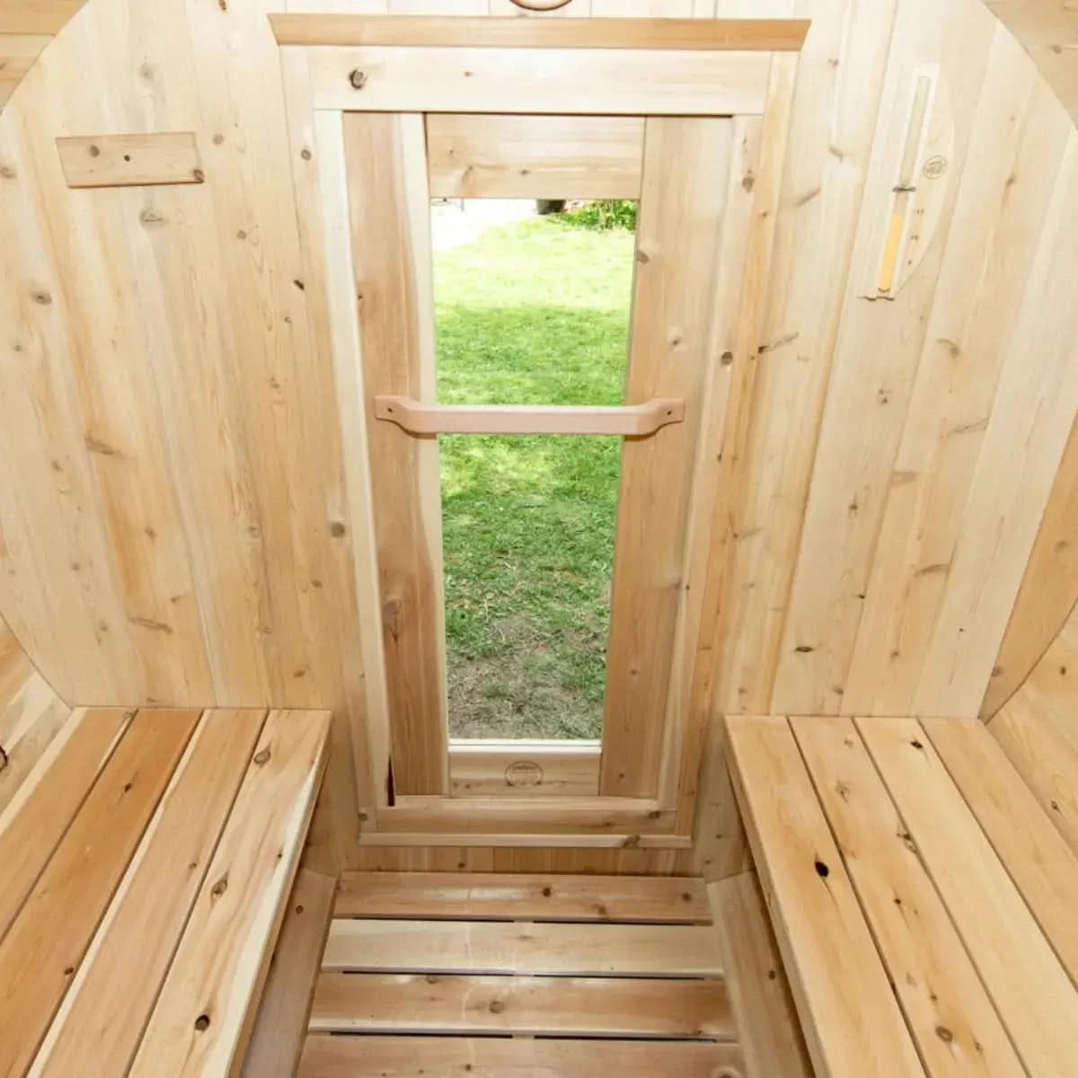 An interior view of a Dundalk LeisureCraft Canadian Timber Harmony Barrel Sauna (CTC22E), showing the open glass door and interior benches.