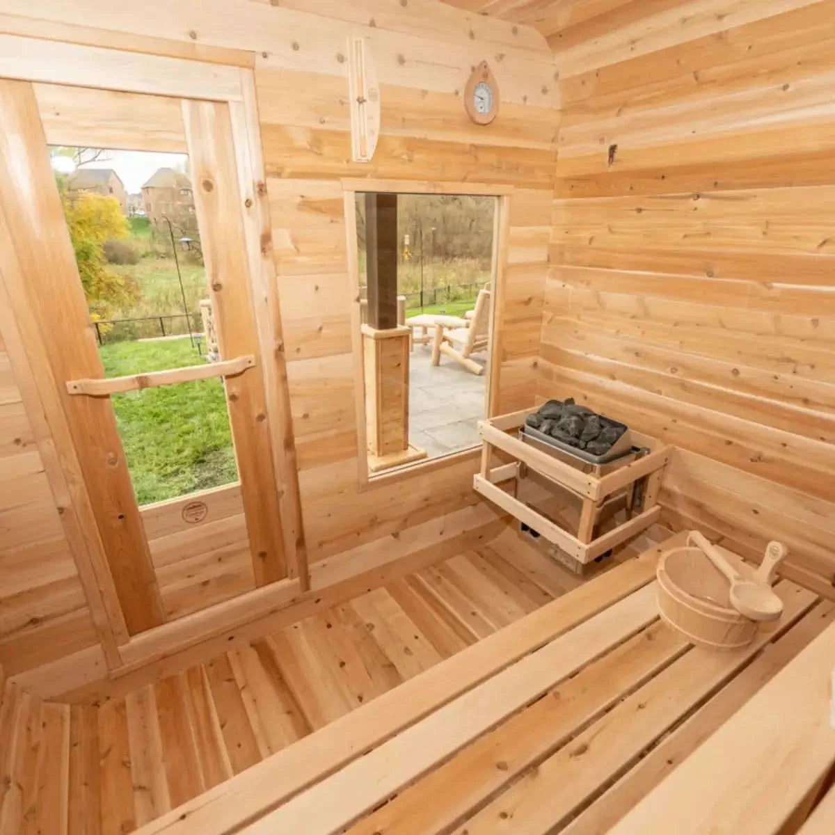 An interior view of a Dundalk LeisureCraft Canadian Timber Luna Sauna (CTC22LU), showing the electric heater, wooden bucket, and view of the outdoors.