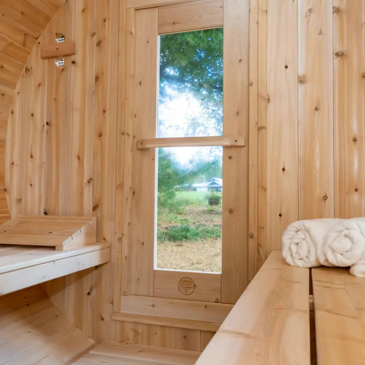Interior view of the Dundalk Leisure Craft CT Serenity Barrel Sauna (CTC2245E), showcasing the cedar wood benches, a large glass door, and the etched Canadian Timber Collection logo.