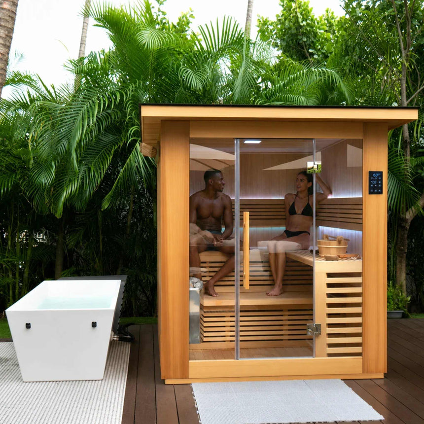 Two people inside the Revive 4 Person Traditional Sauna on an outdoor deck, with the Revive Acrylic Plunge, sold separately, beside it