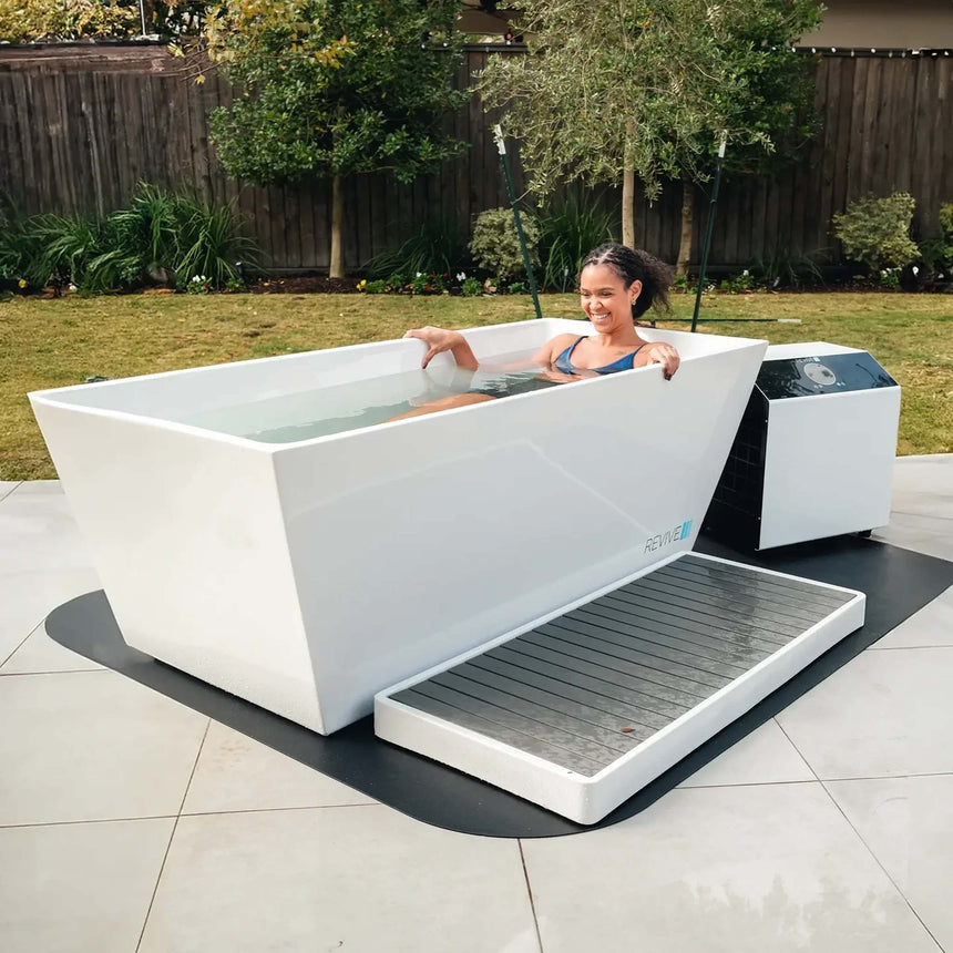 Woman soaking in the Revive Acrylic Plunge in a backyard, shown with the optional Acrylic Basin and protective mat