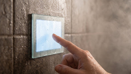 Hand touching a steam shower control touchscreen beaded with condensation