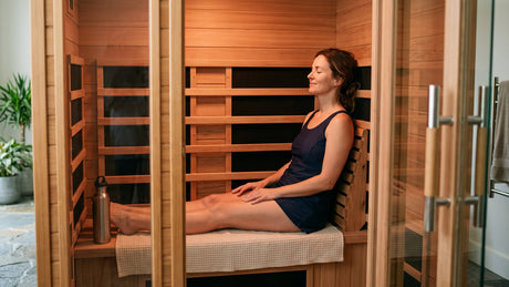 How to use an infrared sauna: an adult seated on a towel with a water bottle nearby