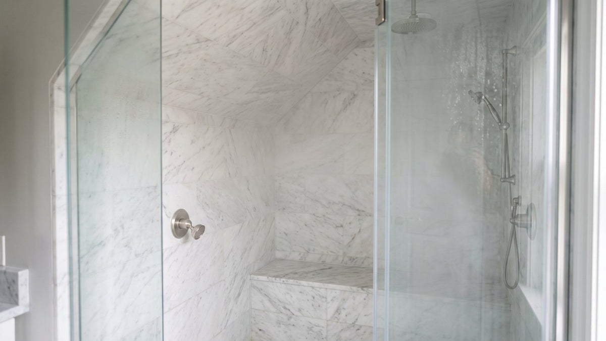 Marble-walled steam shower with a sloped ceiling, gasketed glass door and tiled bench