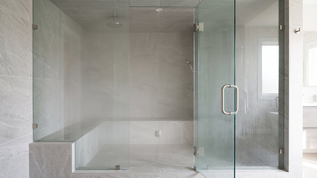 Frameless glass steam shower with large porcelain tiles and a built-in tiled bench filled with light steam