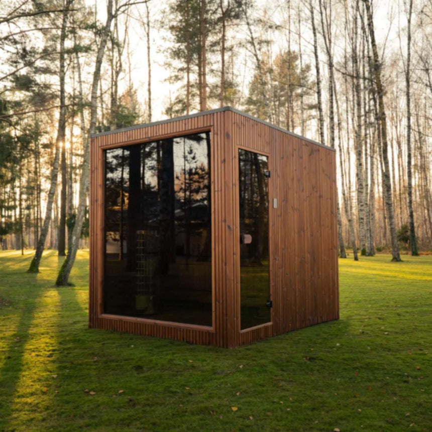 Celsium Jonas Grand outdoor sauna with a bronze-tinted glass front and full-height glass door in a sunlit birch grove