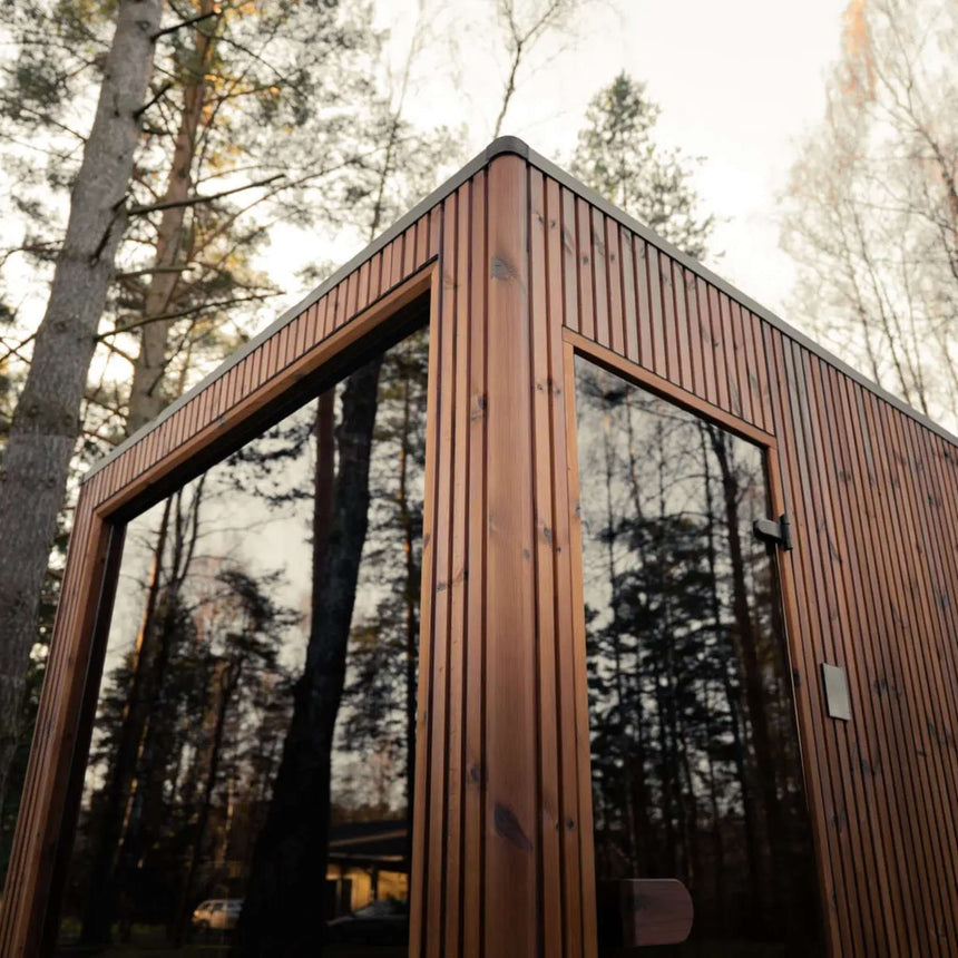 Low-angle view of the Celsium Jonas Grand glass front and glass door reflecting the surrounding pine trees
