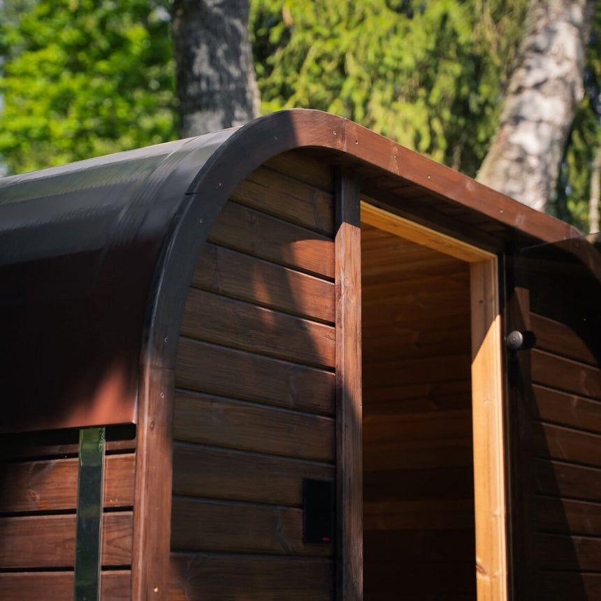 Rounded profile of a brown Celsium Ula Mini outdoor sauna, with a dark roof covering and an open doorway