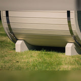 Rounded base of a light-colored Celsium Ula Mini outdoor sauna resting on two supports, with metal bands at each end