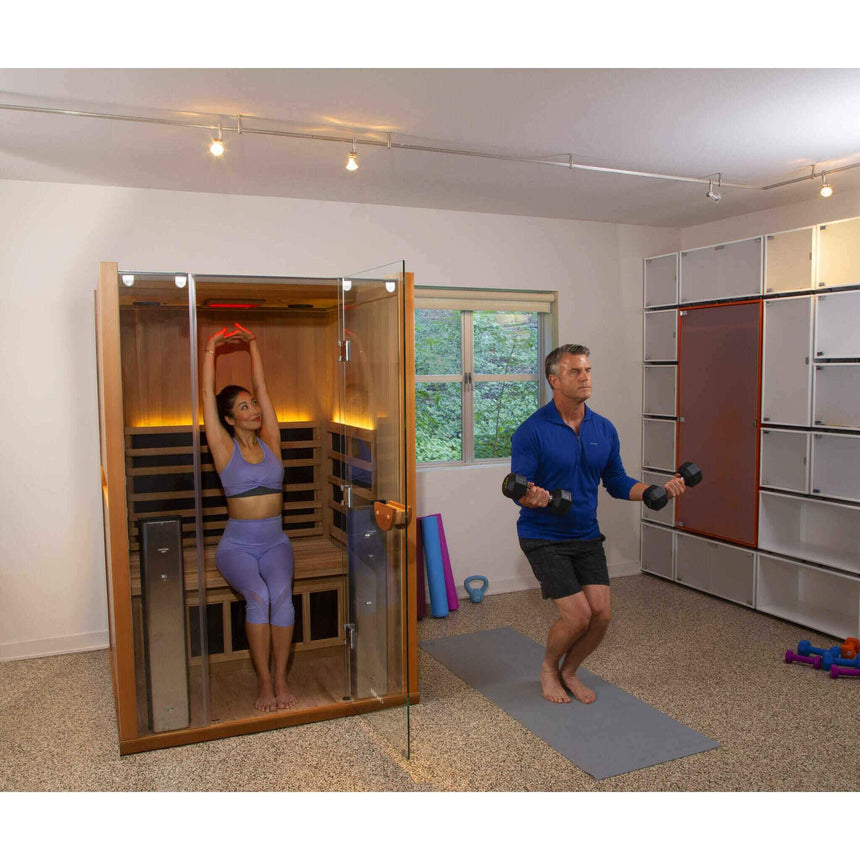 Couple using Clearlight Sanctuary 2 infrared sauna in home gym with fitness equipment