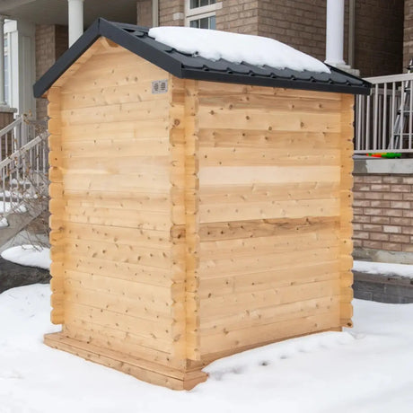 Side exterior view of a Dundalk LeisureCraft Canadian Timber Granby Cabin Sauna (CTC66E) on a snow-covered lawn.