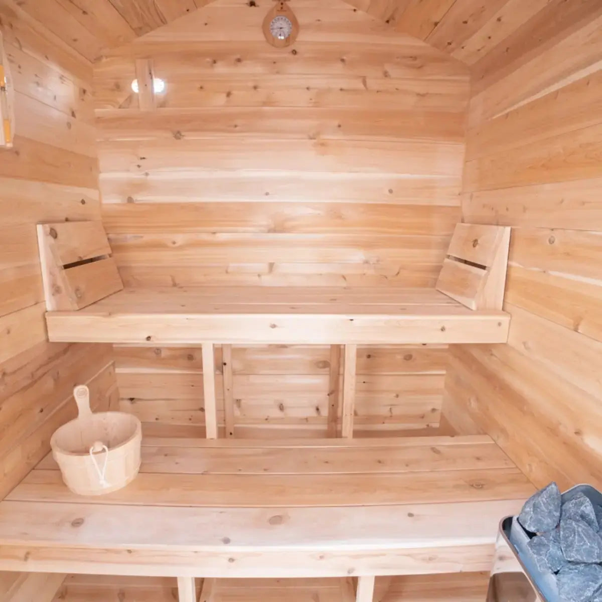 The interior of a Dundalk LeisureCraft Canadian Timber Granby Cabin Sauna (CTC66E), showing the wooden benches, bucket, and ladle.