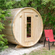 A full exterior view of a Dundalk LeisureCraft Canadian Timber Harmony Barrel Sauna (CTC22E) with a red chair next to it, showing the curved design and entrance.