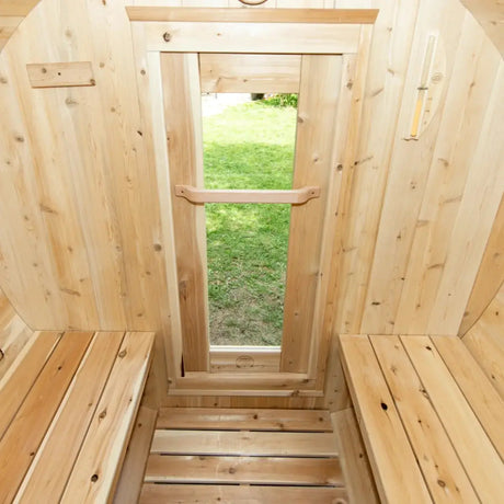 An interior view of a Dundalk LeisureCraft Canadian Timber Harmony Barrel Sauna (CTC22E), showing the open glass door and interior benches.