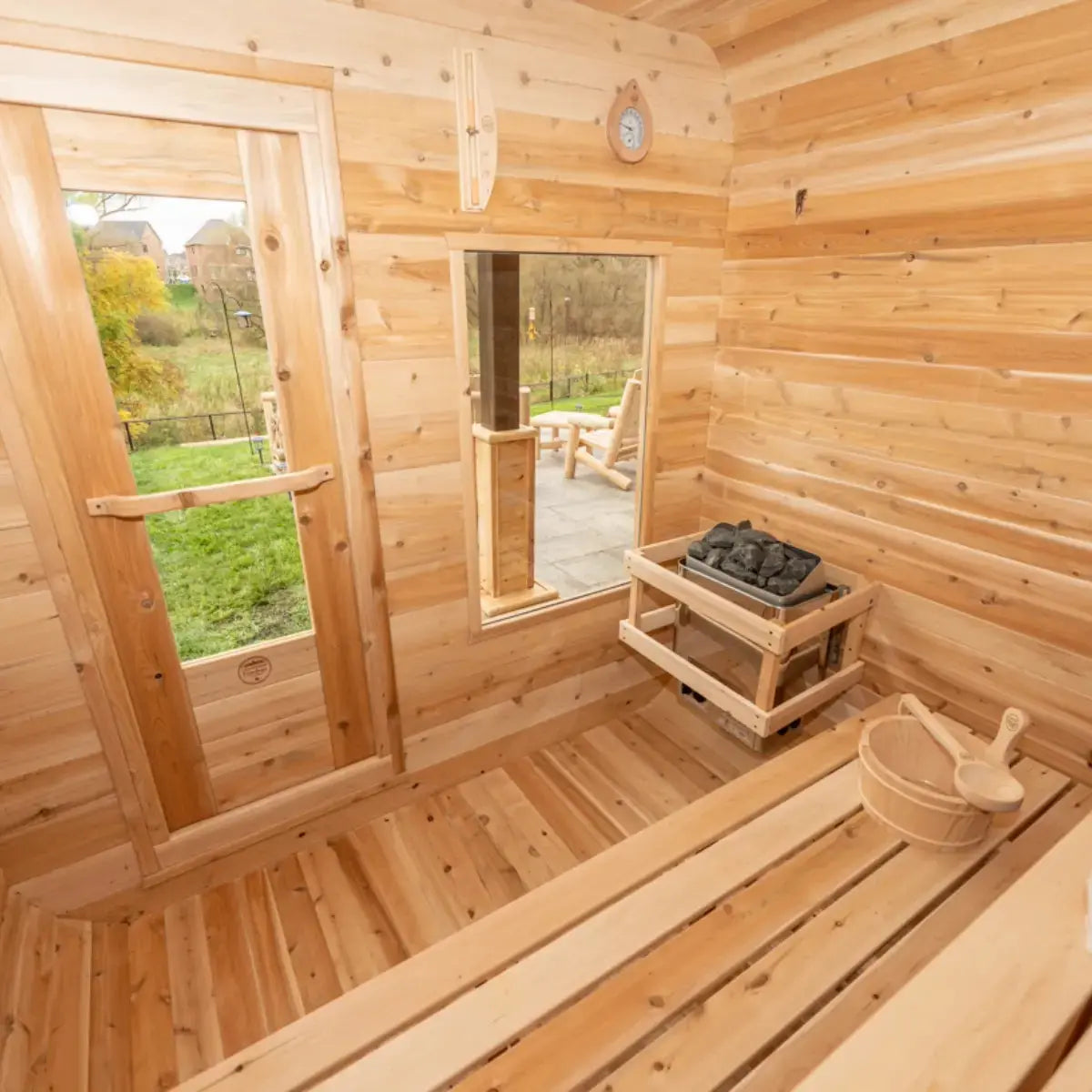 An interior view of a Dundalk LeisureCraft Canadian Timber Luna Sauna (CTC22LU), showing the electric heater, wooden bucket, and view of the outdoors.