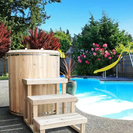 A full view of the Dundalk Leisure Craft Baltic Plunge Tub (CT33BP) with a three-tier wooden step accessory next to it, positioned by a swimming pool in a backyard.