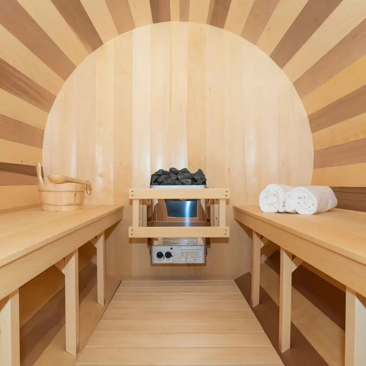 An interior view of the Dundalk Leisure Craft CT Tranquility Barrel Sauna (CTC2345W) with the electric sauna heater, hot stones, and wood benches.