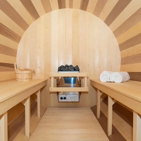 An interior view of the Dundalk Leisure Craft CT Tranquility Barrel Sauna (CTC2345W) with the electric sauna heater, hot stones, and wood benches.