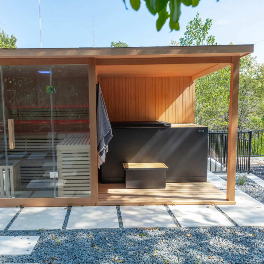 Front view of the covered deck beside the glass front of the Revive 4 Person Traditional Sauna, with the Revive Luxury Plunge, its cover and its step under the deck; the sauna and plunge are sold separately