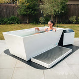 Woman soaking in the Revive Acrylic Plunge in a backyard, shown with the optional Acrylic Basin and protective mat