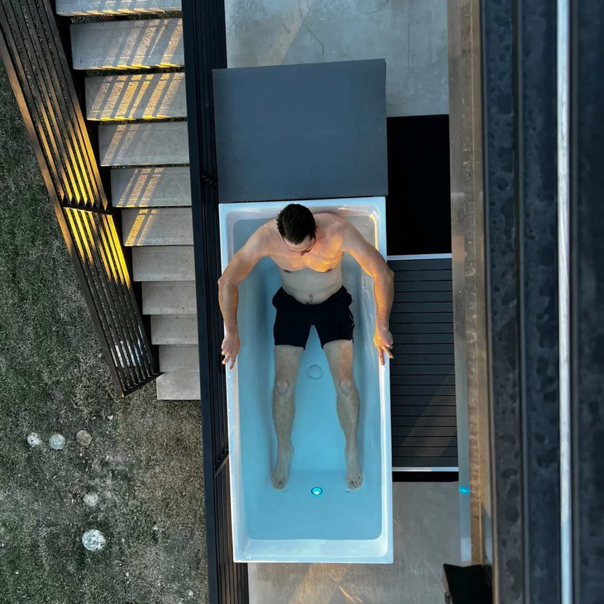 Top view of a man in the Revive Acrylic Plunge with the LED tub light on, beside the optional Acrylic Basin