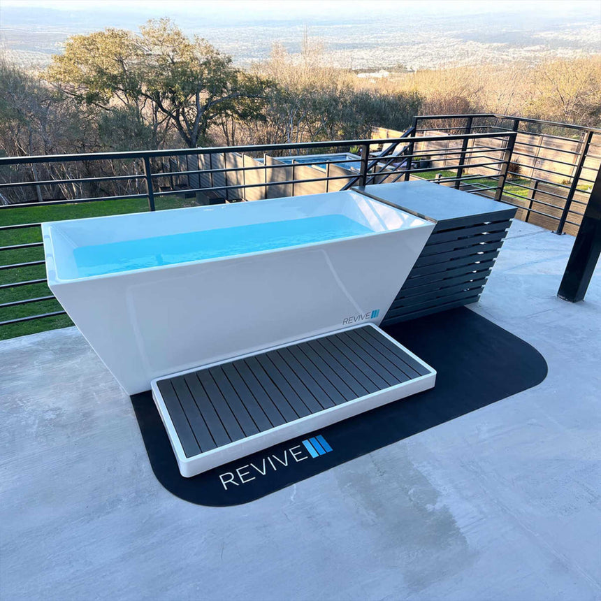 Revive Chiller Cover at the end of a water-filled Revive Acrylic Plunge on a terrace, with the Revive Acrylic Basin on a protective mat in front; the plunge, basin and mat are sold separately