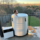 Man soaking in the Revive Inflatable Barrel Plunge on a terrace at sunset, with the chiller and step beside it