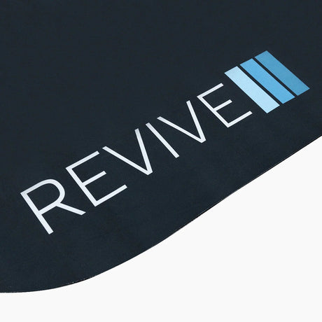Close-up of the white and blue Revive logo near a corner of the Revive Padded Protective Mat
