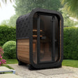 SaunaLife Model CL3G 2-person outdoor cube sauna with black hexagonal roof and natural wood panel in landscaped backyard setting.