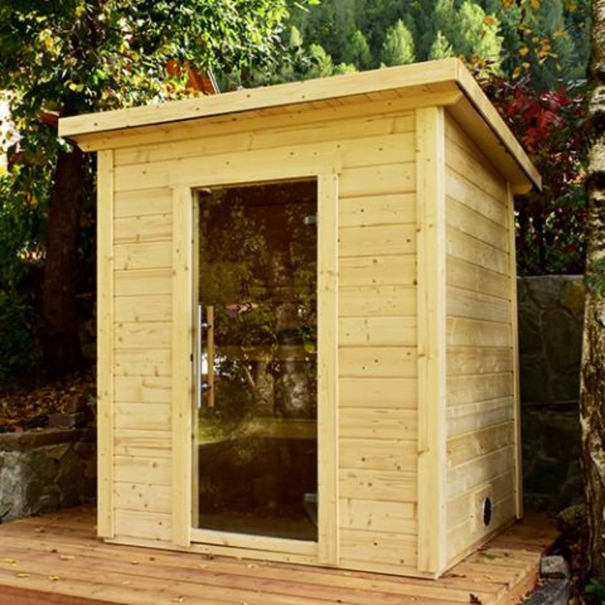 SaunaLife Model G2 4-person outdoor sauna installed in backyard garden with clear tempered glass door and slanted roof.