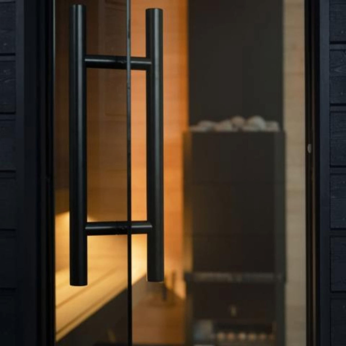 SaunaLife G6 Garden Series outdoor sauna entrance with double-glazed clear glass door and black aluminum handle at dusk.