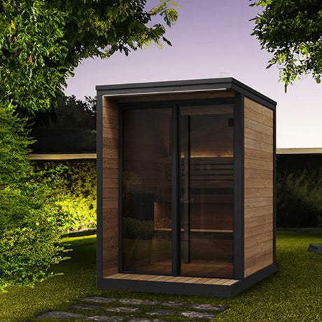 SaunaLife Model GL4 4-person Garden Luxury outdoor sauna at night with LED eaves lighting, bronze glass front and black trim.