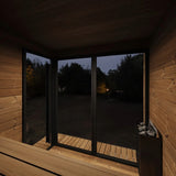 SaunaLife Model GL6 Garden Luxury sauna interior view at dusk through bronze glass windows showing thermo-spruce walls and benches.